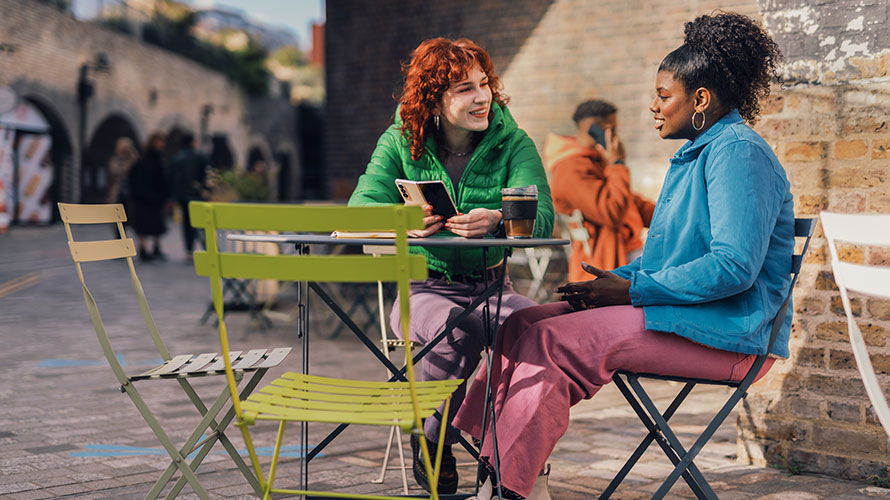 Two Women Talking By A Table With Coffee By A Table